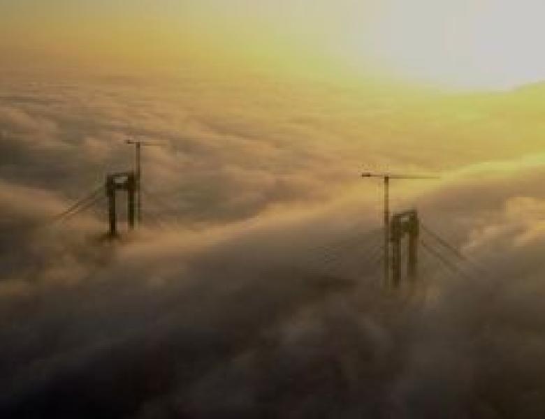 A ponte de Rande en obras e inmersa na néboa da ría no solpor.